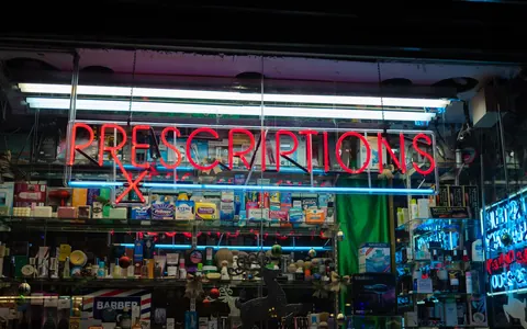 An illuminated pharmacy sign advertising prescriptions above a storefront at night