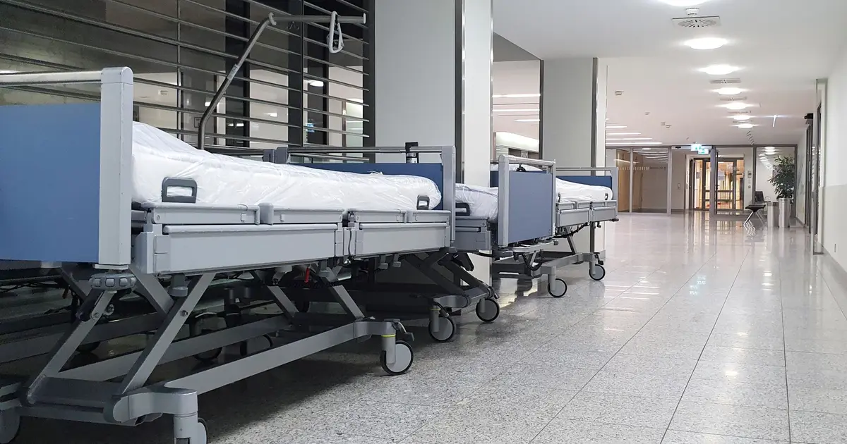 Quiet hospital hallway with neatly arranged empty medical beds under bright ceiling lights