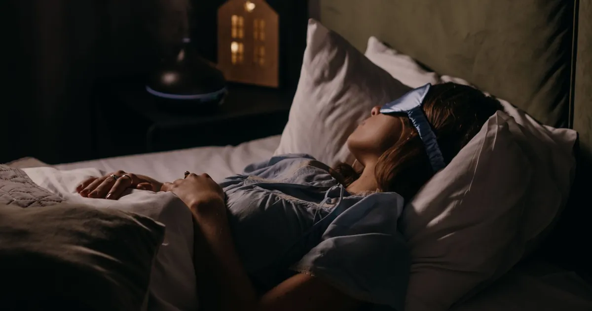 A woman asleep wearing an eye mask in a dim bedroom