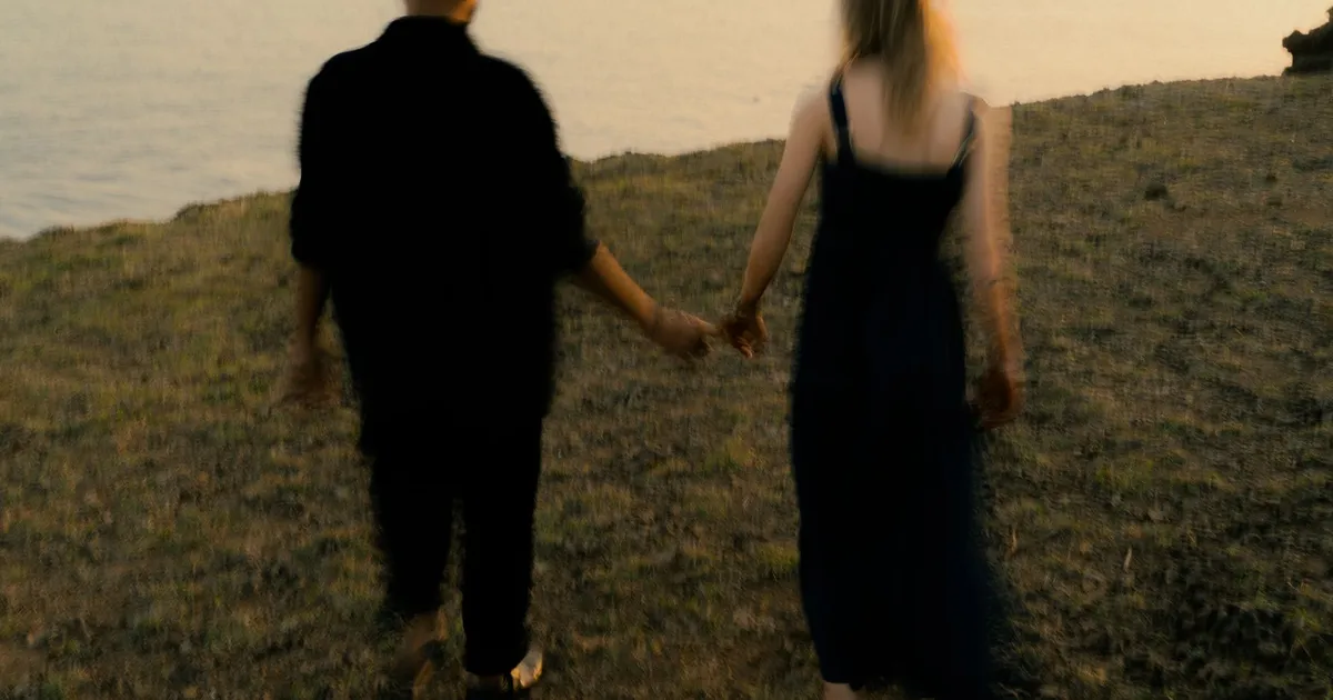 A couple walking hand in hand by a lake at sunset