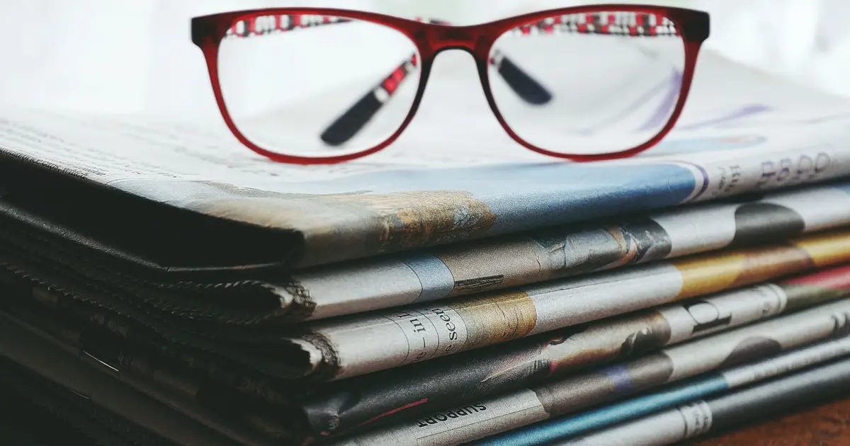 Red eyeglasses resting on a stack of newspapers symbolize reading and information