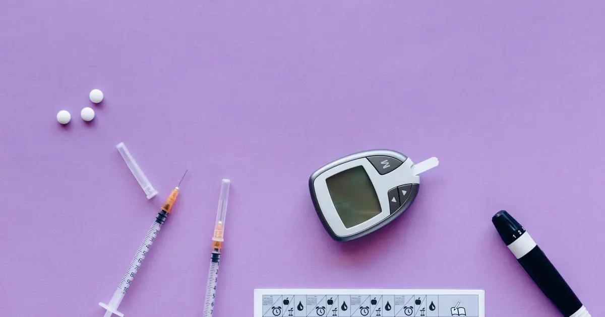 Diabetes management tools laid out on a flat surface: a glucose meter, syringes and tablets