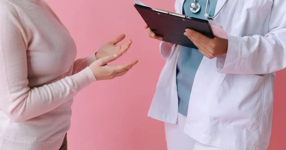 A patient talking with a doctor who holds a clipboard