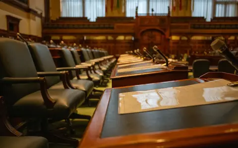A detailed view of an empty legislative chamber with rows of desks and microphones, evoking governance