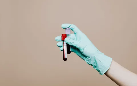 A gloved hand holding a blood sample tube in a lab