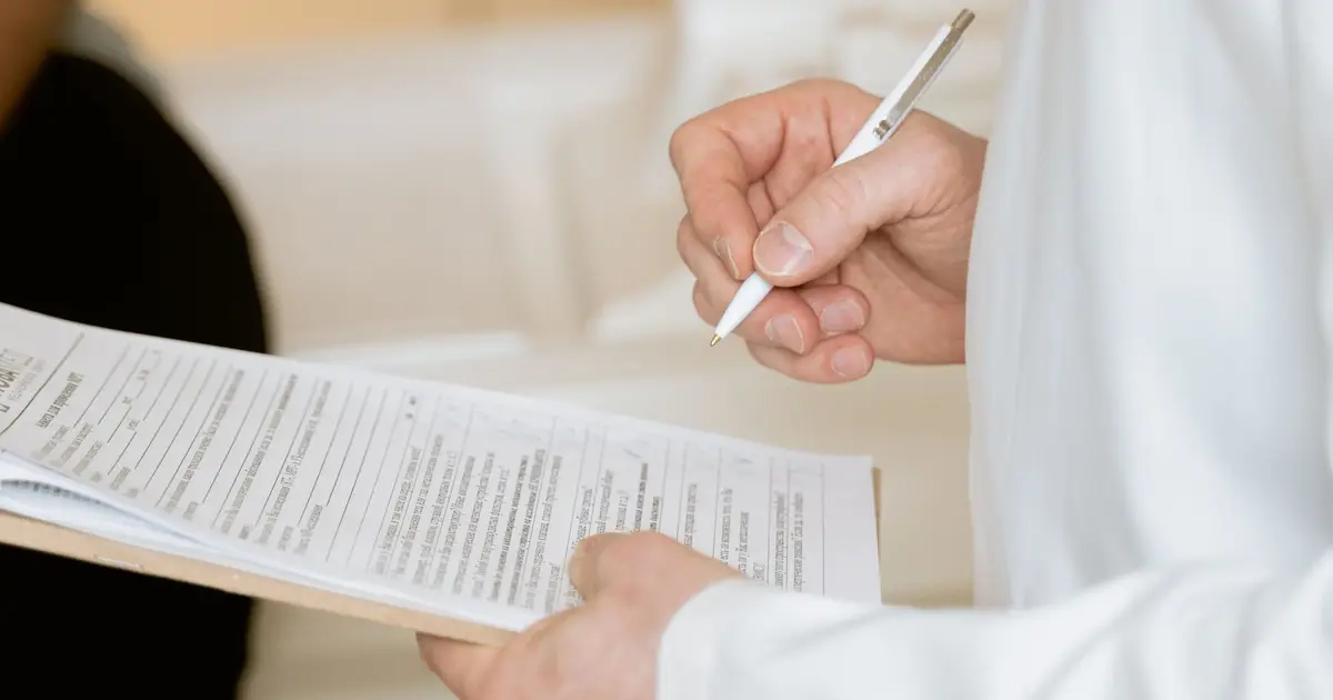 A medical professional in a white coat examines a clipboard with patient documents
