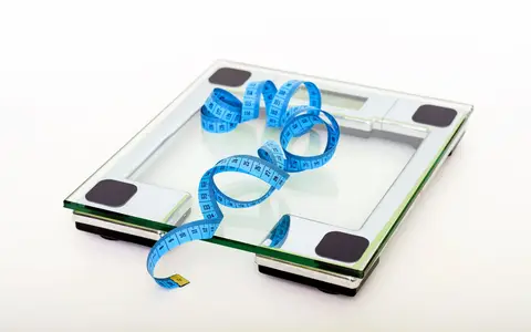 A glass bathroom scale with a blue measuring tape lying on it