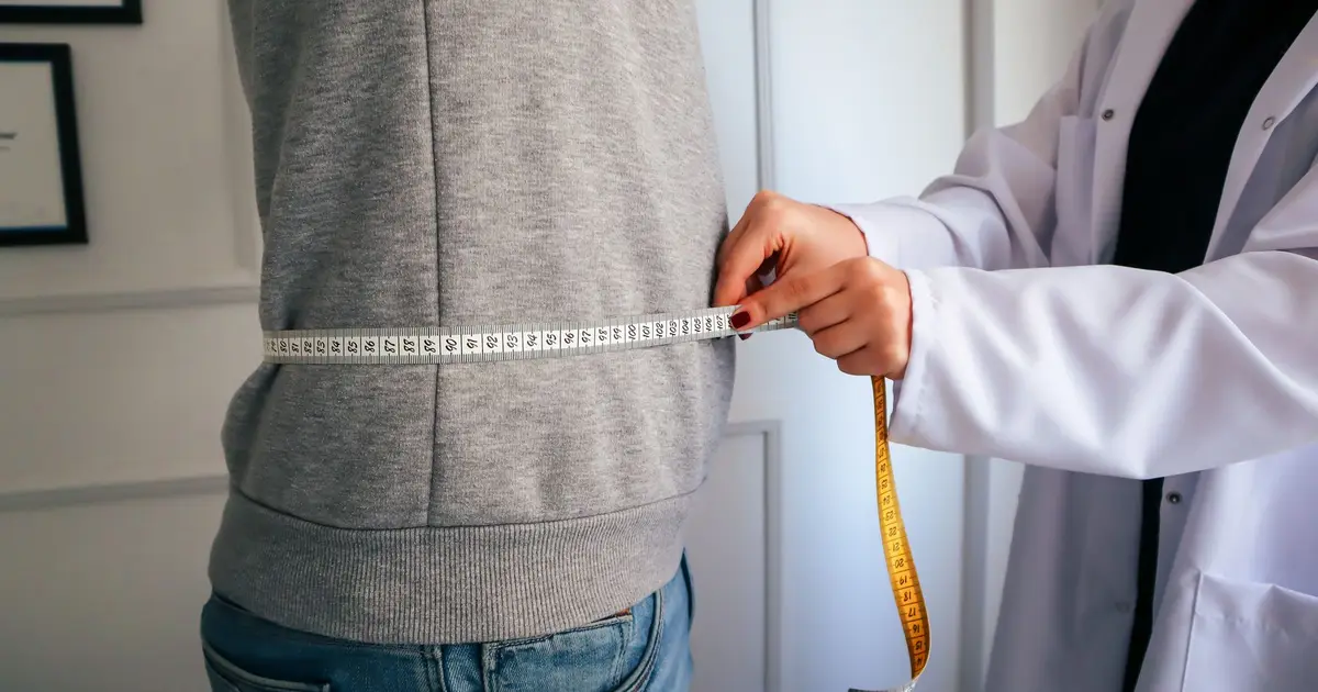 A nutritionist measuring a patient's waist using a tape in a clinical setting