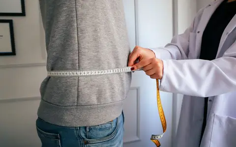 A nutritionist measuring a patient's waist using a tape in a clinical setting