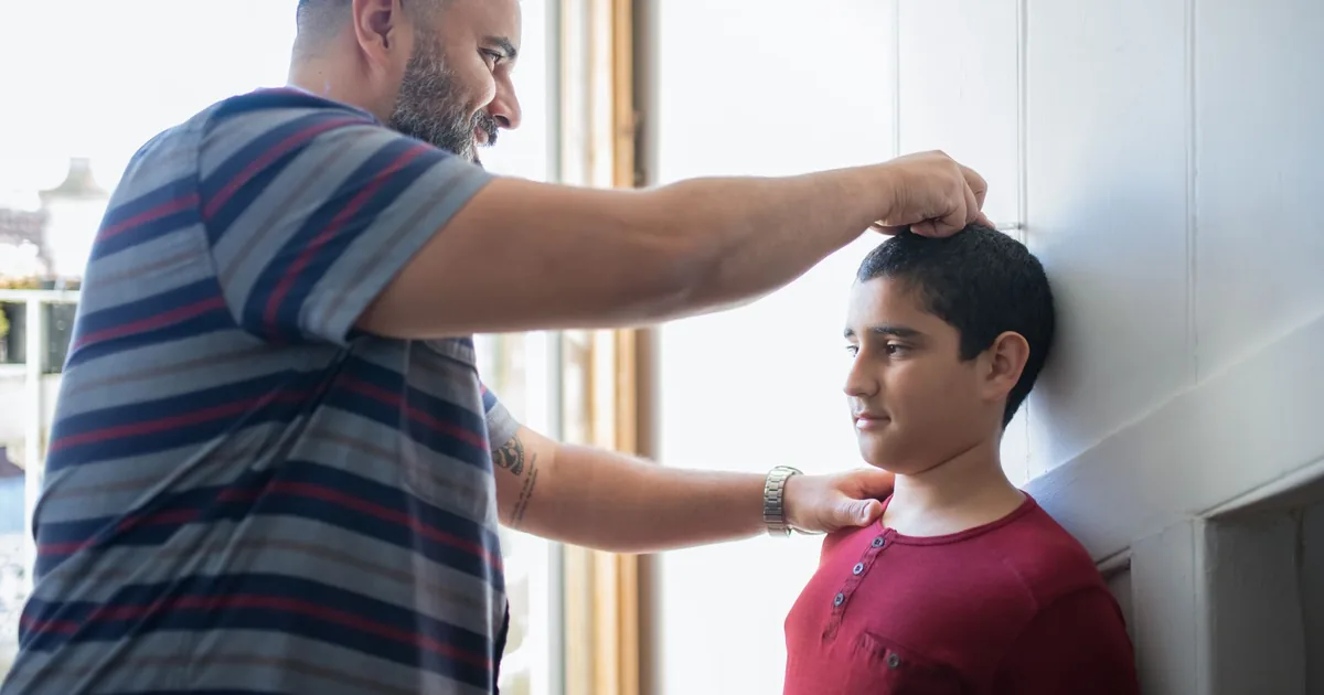 A father measuring his son's height against a wall at home