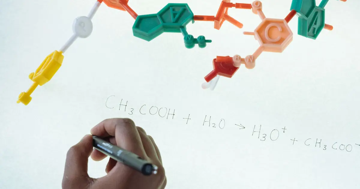 Anonymous chemist writing with marker on illuminated magnetic board formula of Hydronium and Acetate production after studying plastic model of molecule in laboratory